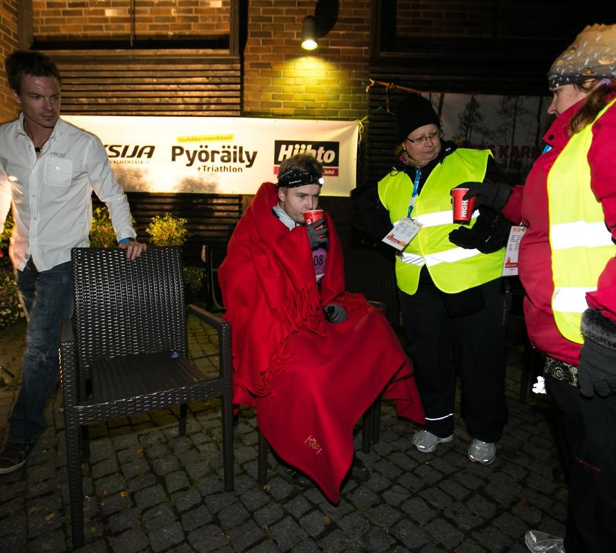 Vaarojen Maratonin talkoolaiset huolehtimassa juoksijoista tapahtumapaikalla pime&auml;ss&auml; illassa, tarjoten huoltoa ja l&auml;mp&ouml;&auml; kilpailijoille.
