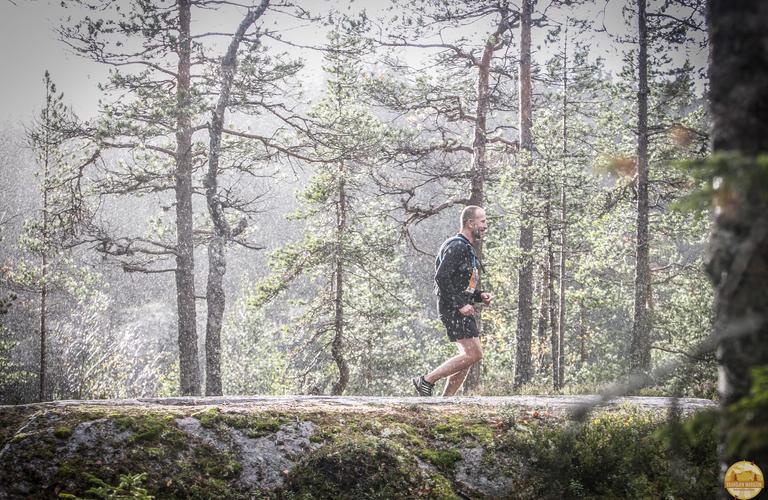 Vaarojen Maratonin juoksija etenemässä polulla Kolin kansallispuiston metsämaisemassa, ympärillään sateinen ja vehreä luonto.