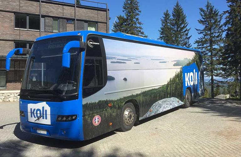 Vaarojen Maratonille saapuvien juoksijoiden linja-auto pysäköitynä Kolin kansallispuistossa, taustalla metsäiset maisemat.