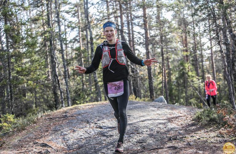 A Vaarojen Maraton runner smiling in the heart of nature, gliding along a rocky trail through the forest landscapes of Koli National Park.