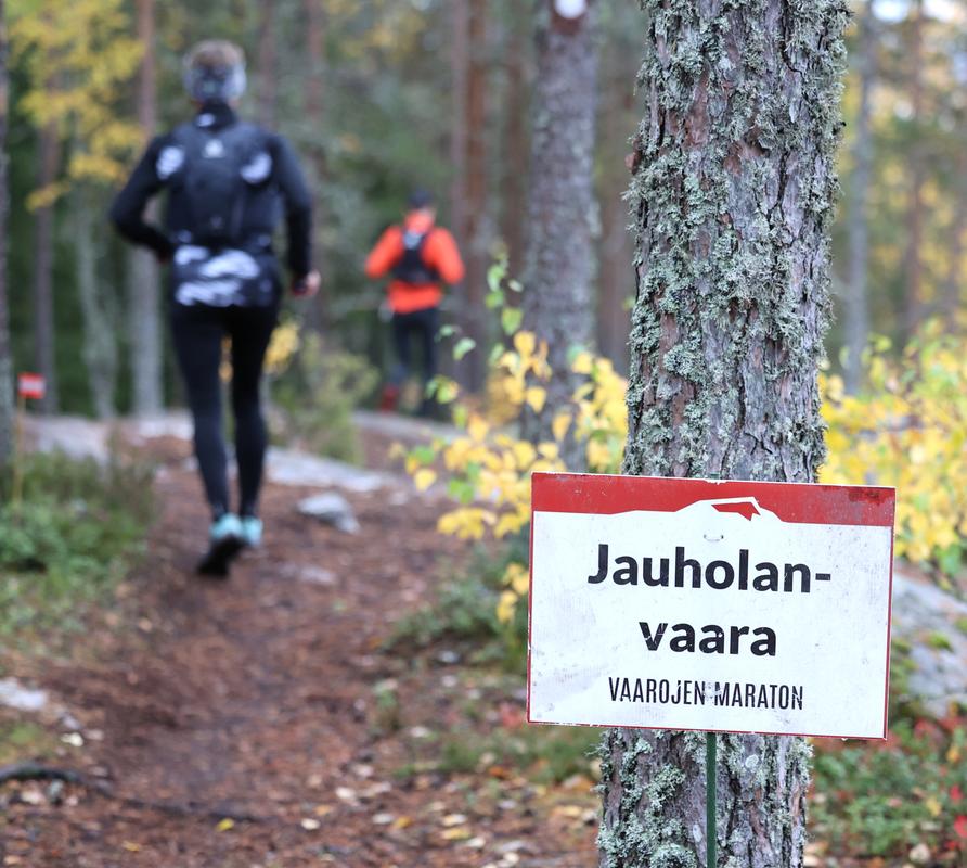 Vaarojen Maratonin polkujuoksijat Jauholanvaaran reitillä, reittimerkki opastamassa syksyisessä metsämaisemassa.